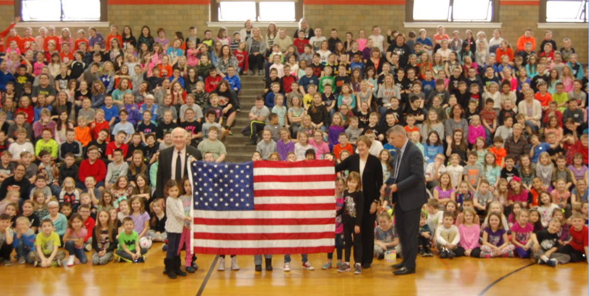 people holding a flag in a gymnasium full of students